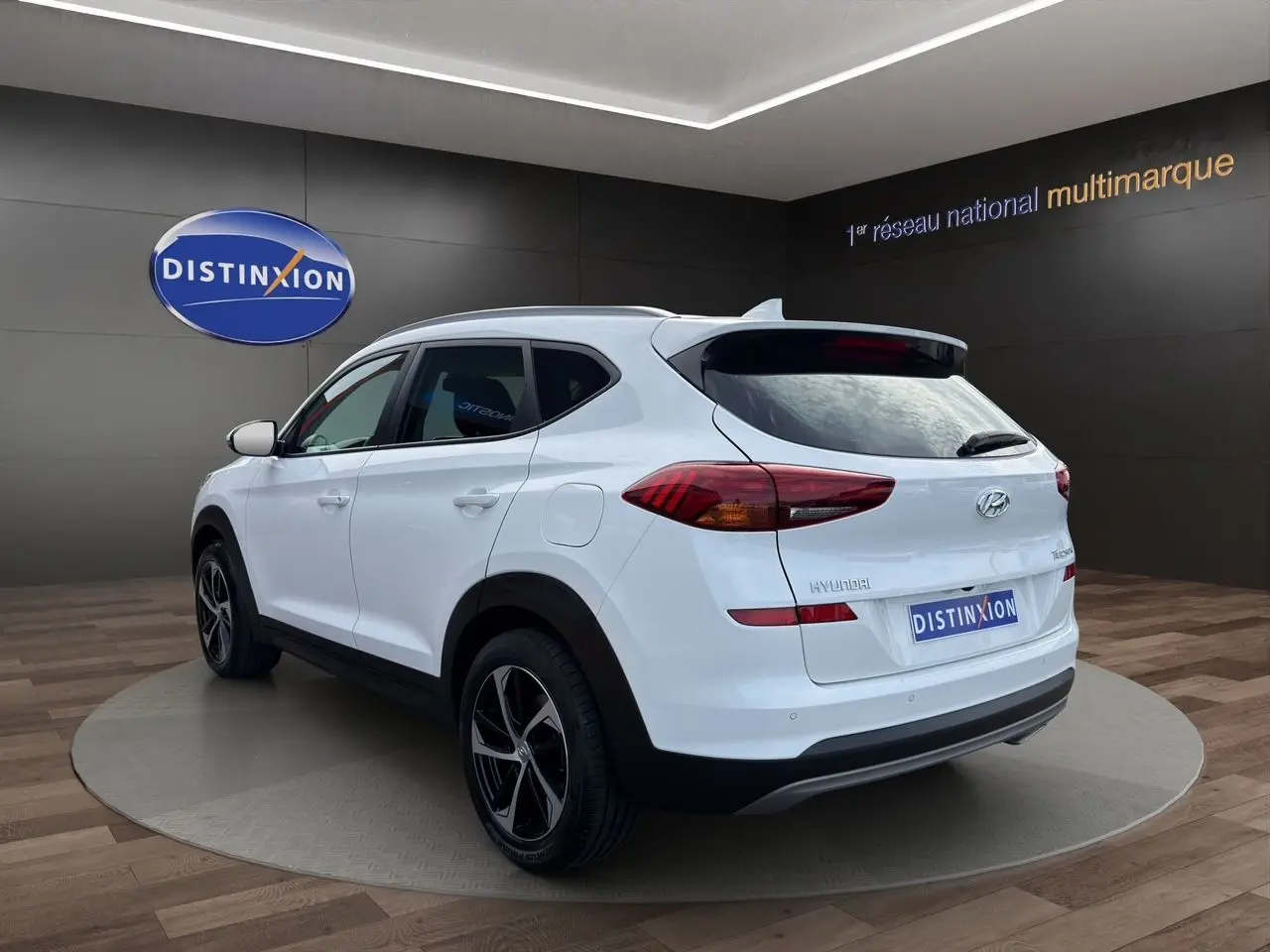 Vue 3/4 arrière droite du Hyundai Tucson blanc polar 2020 avec jantes 18 pouces bicolores dans un showroom.