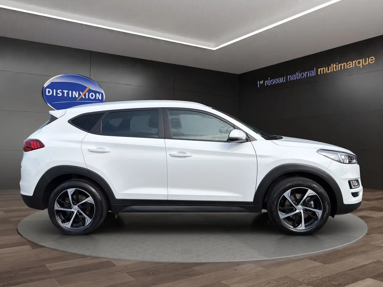 Vue de profil côté gauche d'un Hyundai Tucson blanc polar avec jantes 18 pouces bicolores dans un showroom.