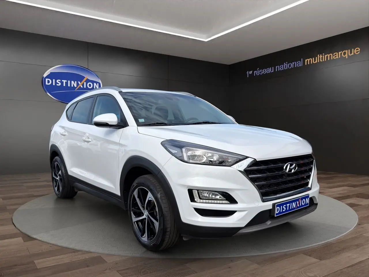 Hyundai Tucson blanc polar en 3/4 avant droit, avec jantes 18 pouces bi-ton et calandre noire distinctive.