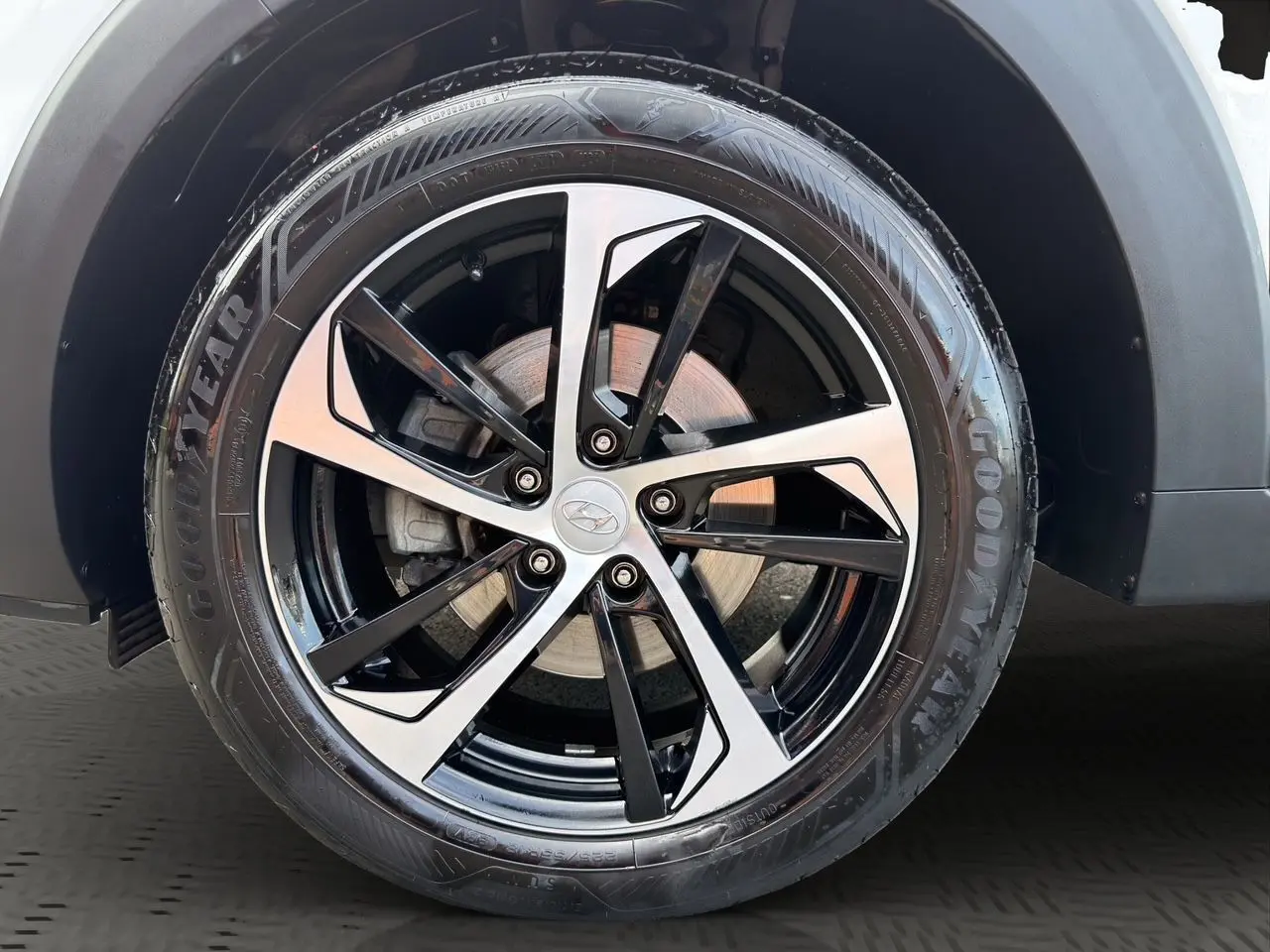 Gros plan sur la jante 18 pouces bicolore noire et argent d’un Hyundai Tucson blanc polar avec pneu Goodyear.
