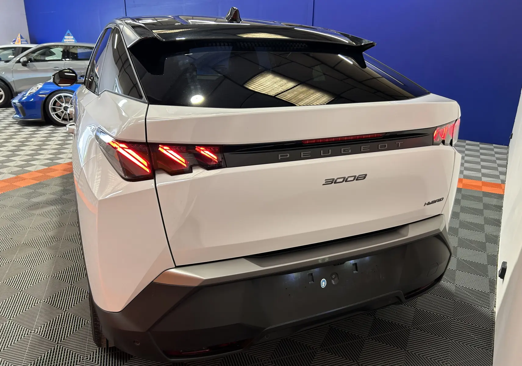 Vue 3/4 arrière droite du Peugeot 3008 blanc Okenite avec feux LED allumés et hayon électrique en intérieur showroom.
