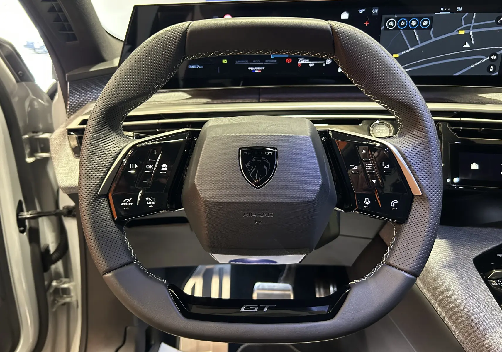 Vue rapprochée du volant cuir perforé noir du Peugeot 3008 III Hybrid 145 GT avec tableau de bord numérique et démarrage sans clé.