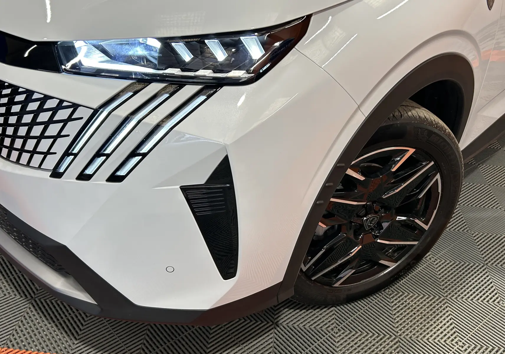 Gros plan sur l’avant droit blanc Okenite du Peugeot 3008 III Hybrid avec phares LED et jante noire brillante.