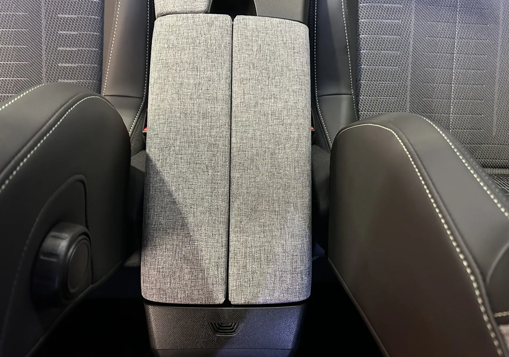 Vue rapprochée de l'accoudoir central tissu gris entre les sièges avant en cuir noir du Peugeot 3008 hybride 2025.