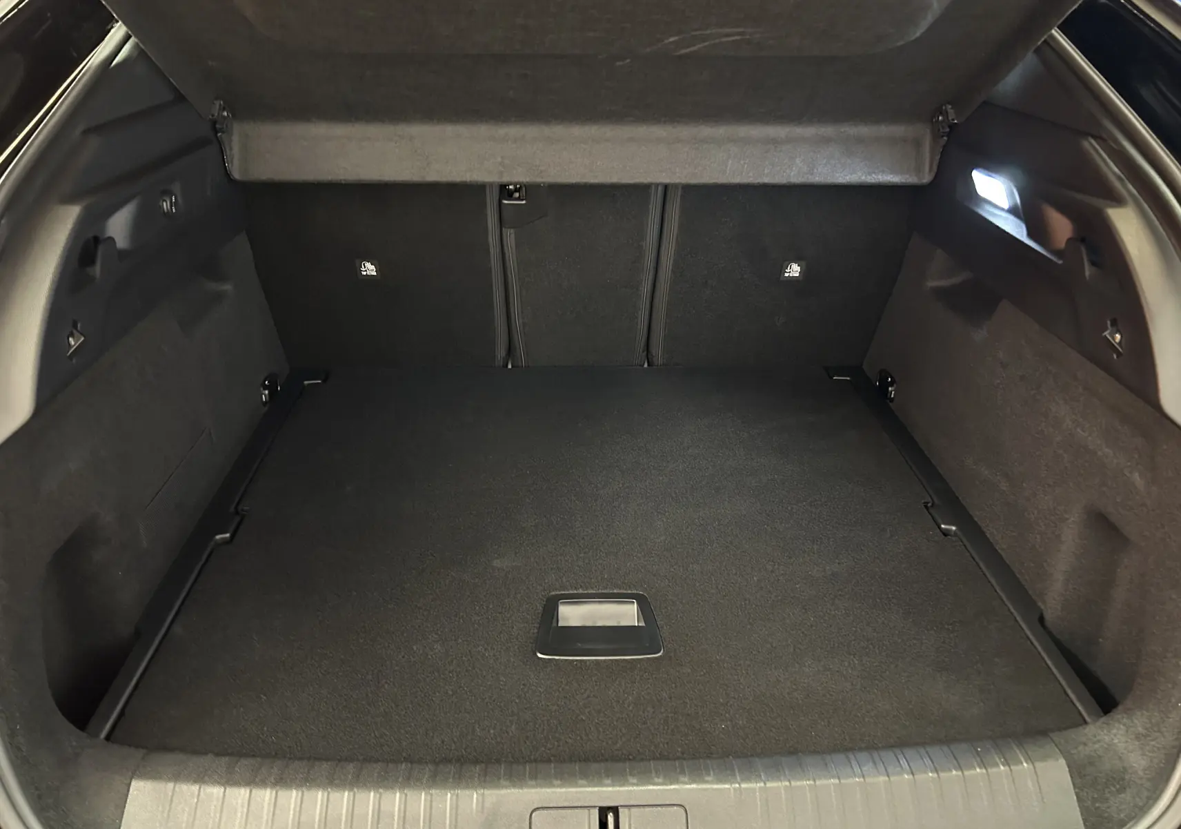 Coffre ouvert vu de l’arrière d’un Peugeot 3008 III Hybrid blanc, avec hayon électrique et intérieur noir.