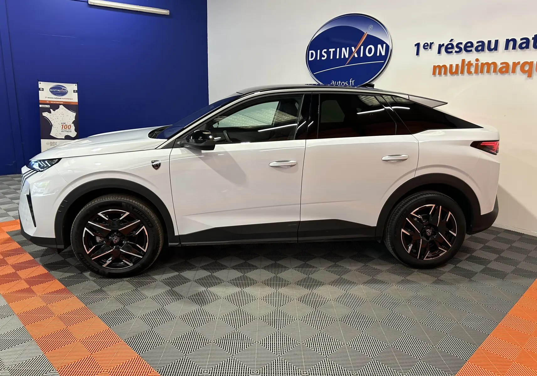Vue de profil côté gauche du Peugeot 3008 III Hybrid blanc Okenite avec jantes noires et toit noir en intérieur showroom.