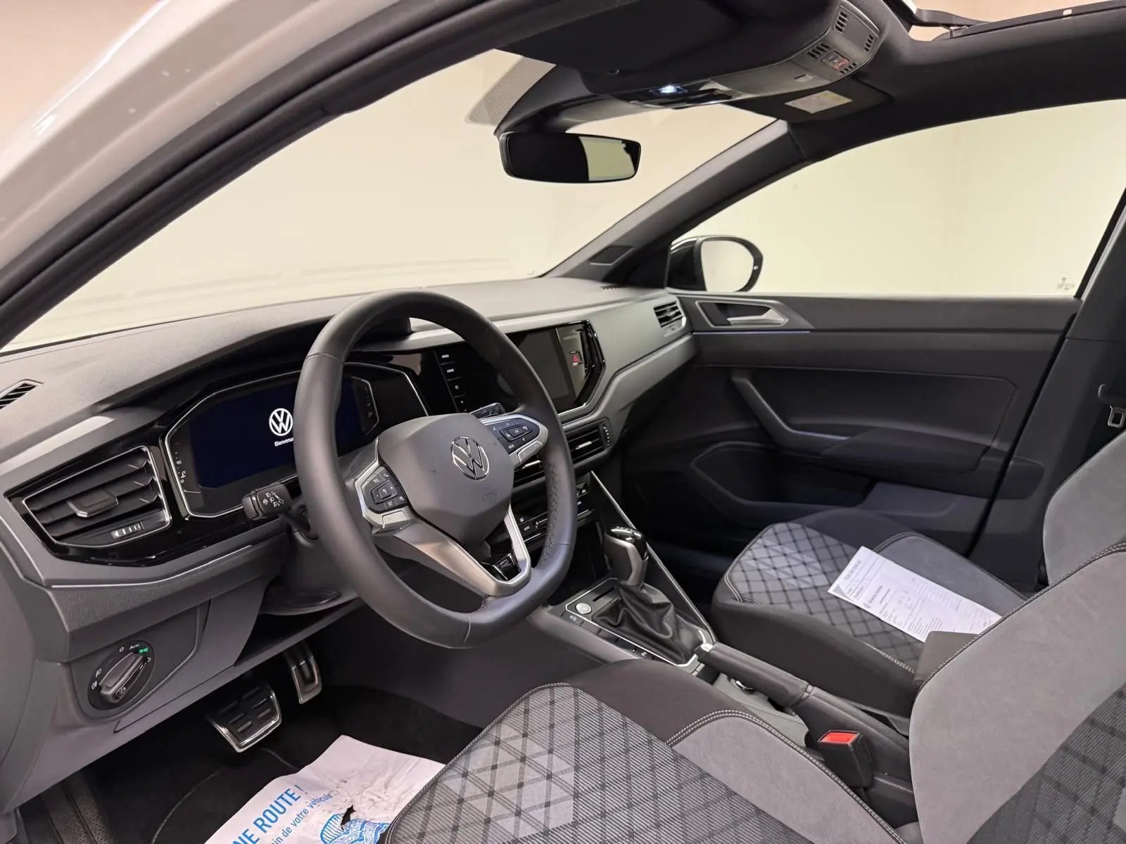 Vue intérieure côté conducteur du Volkswagen Taigo blanc pur, avec tableau de bord digital et sièges tissu gris à motifs.