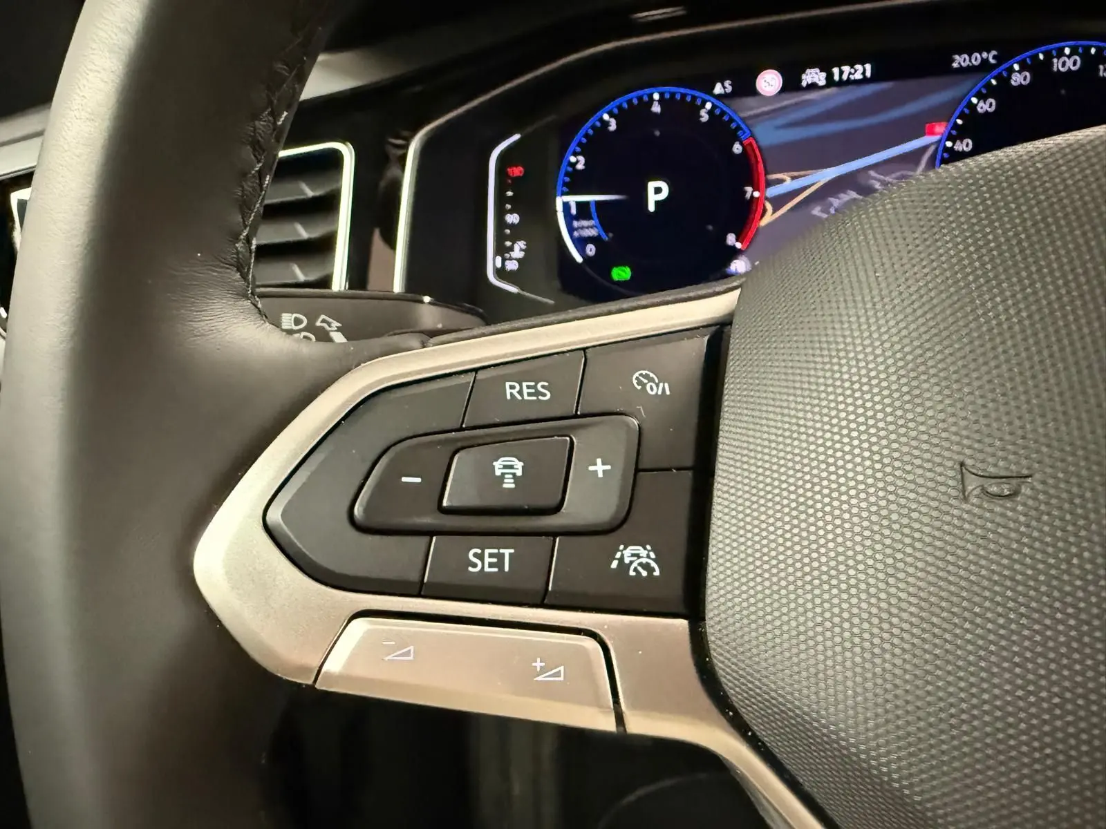 Gros plan sur les commandes multifonctions à gauche du volant cuir du Volkswagen Taigo blanc, affichage digital en arrière-plan.