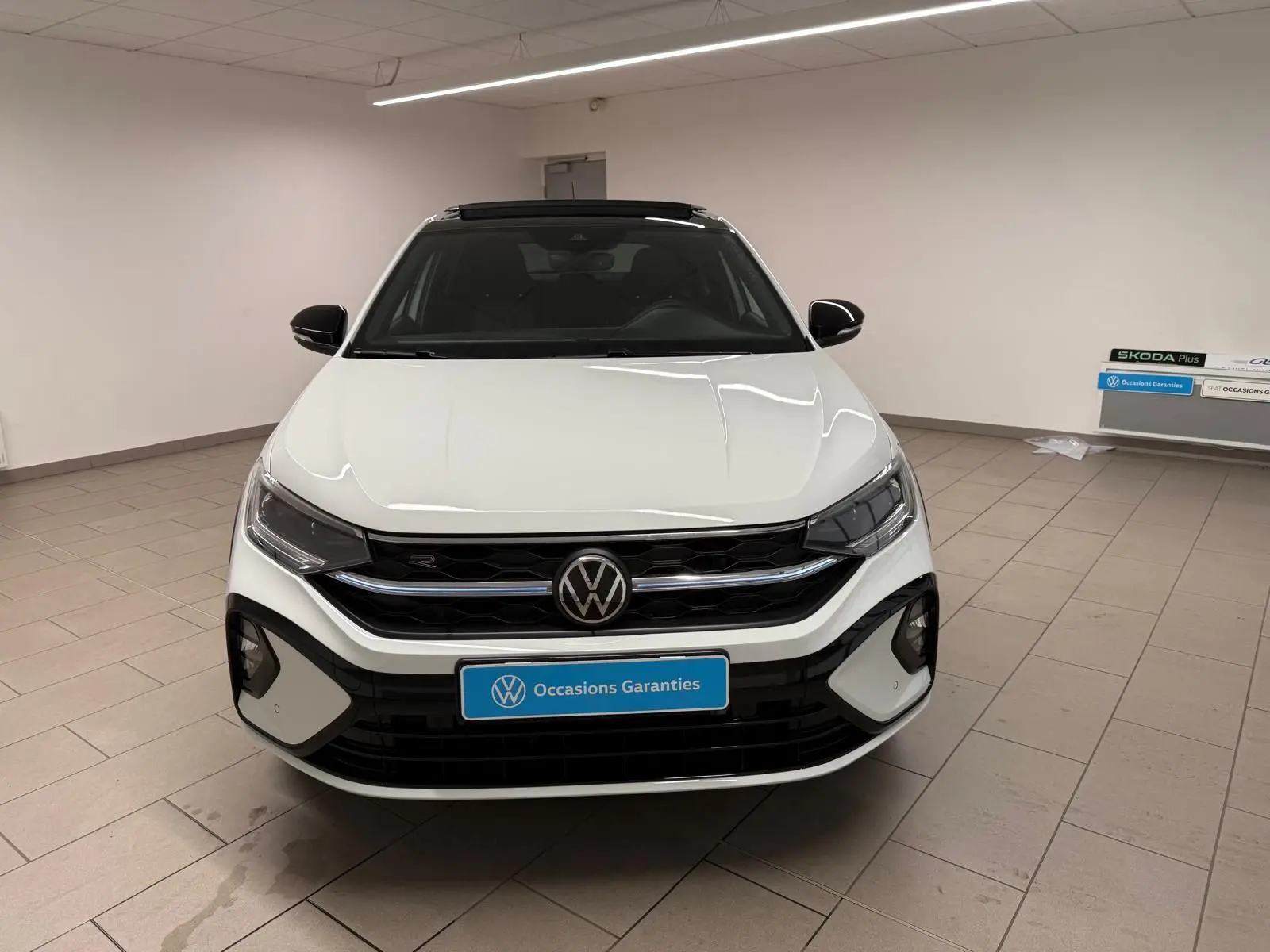 Vue de face d'un Volkswagen Taigo blanc pur avec toit noir, calandre R-Line et éclairage LED dans un showroom.