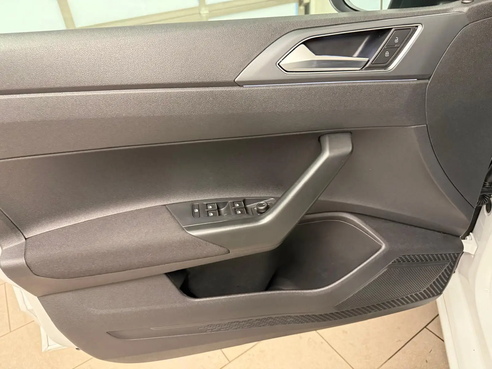 Vue rapprochée de la porte avant gauche du Volkswagen Taigo blanc pur, montrant les commandes de vitres et la poignée intérieure grise.