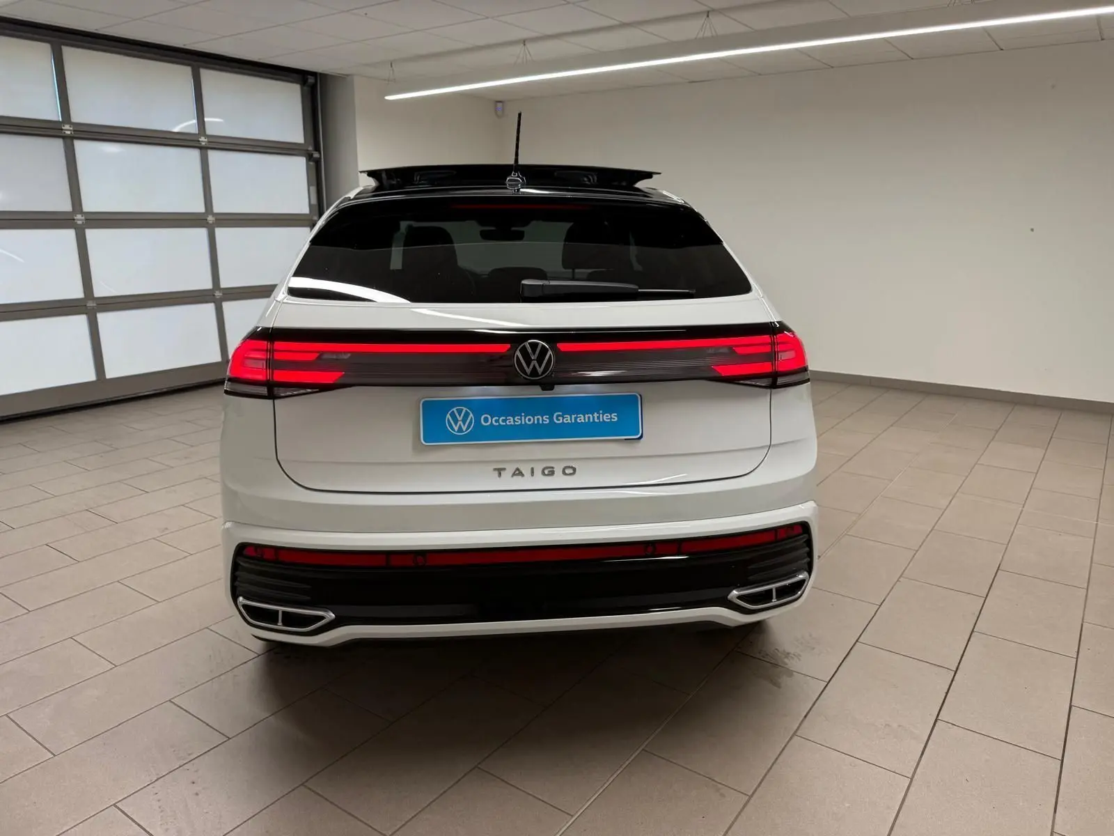 Vue arrière d'un Volkswagen Taigo blanc pur avec toit noir et feux arrière LED allumés en intérieur.