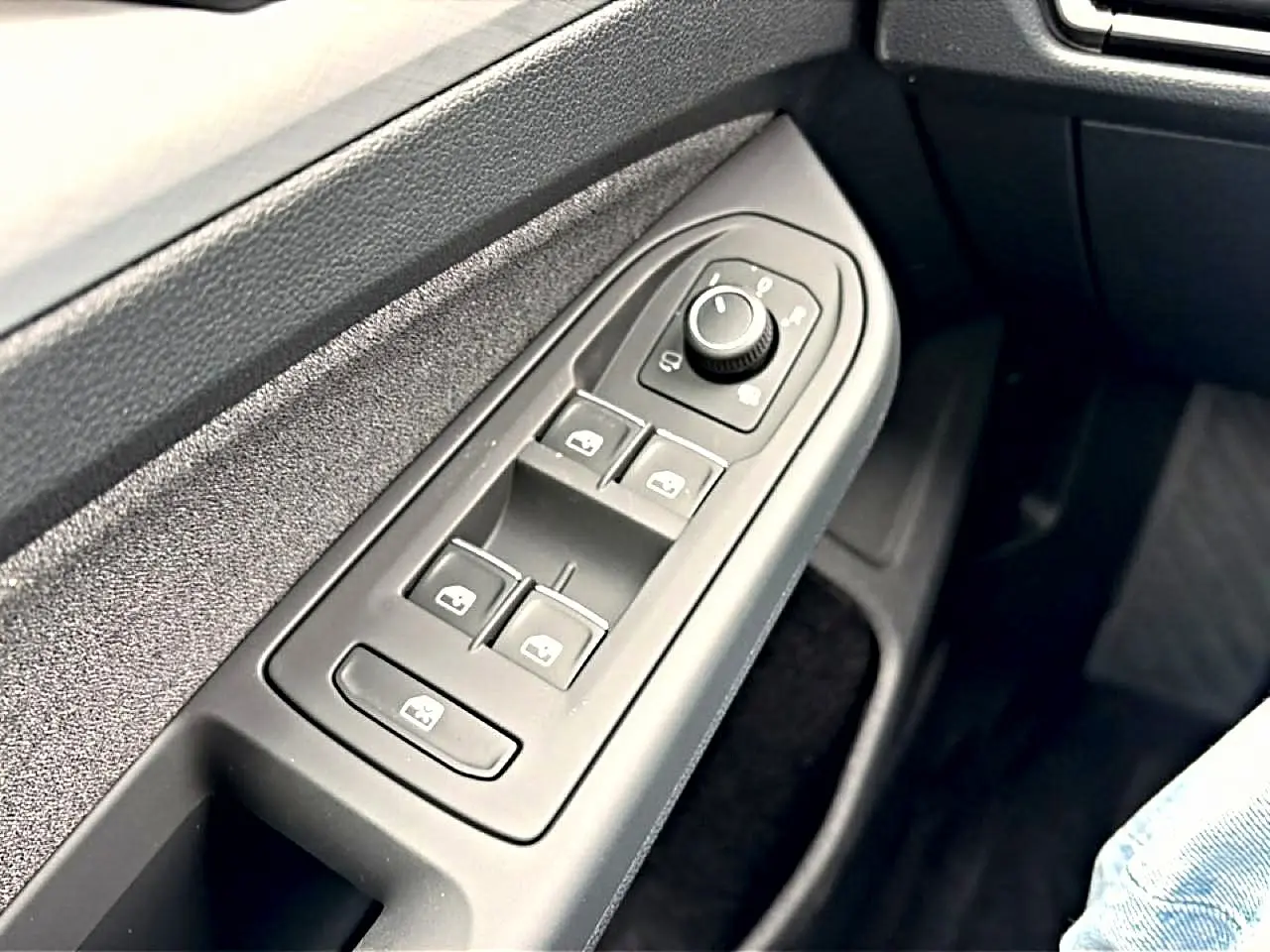 Gros plan sur les commandes des vitres et rétroviseurs côté conducteur d'une Volkswagen Golf bleu glacier.