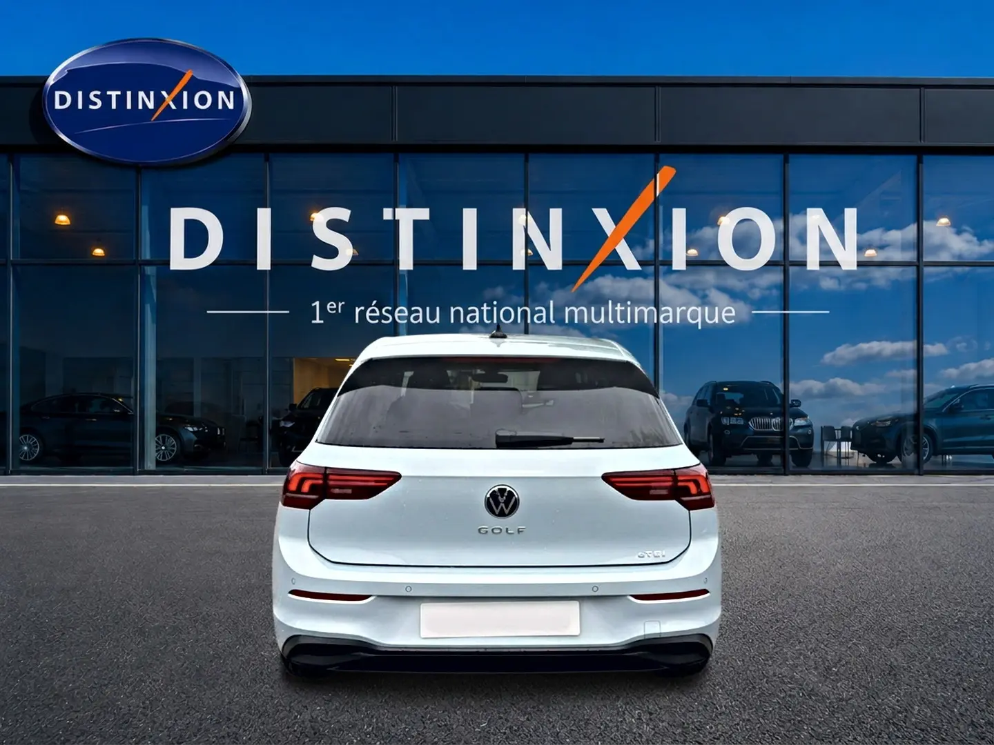 Vue arrière d'une Volkswagen Golf blanche stationnée devant une vitrine avec logo Distinxion visible.