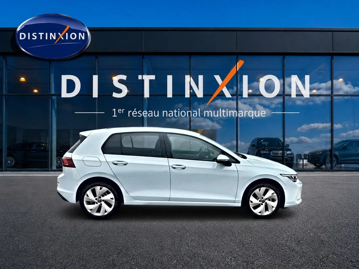 Vue de profil côté gauche d'une Volkswagen Golf 2026 bleu glacier garée devant une vitrine avec logo Distinxion.