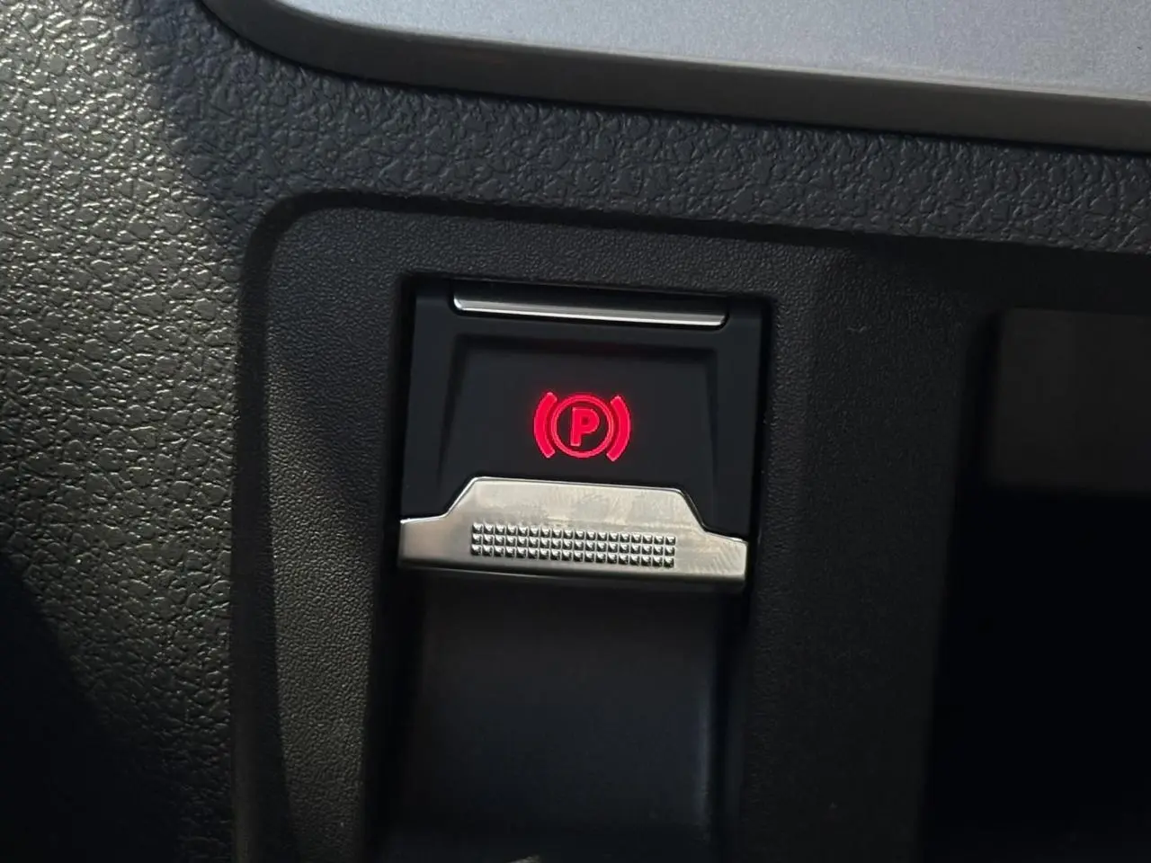Gros plan sur le bouton de frein de stationnement électrique avec témoin rouge dans l'habitacle du Citroën Jumpy noir Perla.