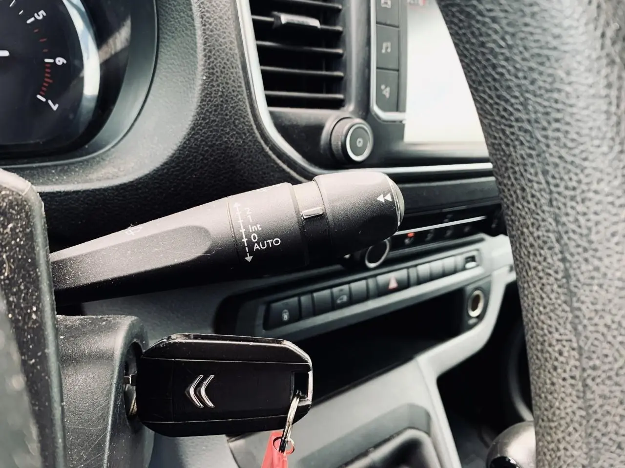 Vue rapprochée du tableau de bord et clé de contact du Citroën Jumpy XL blanc, avec commandes et volant partiellement visibles.