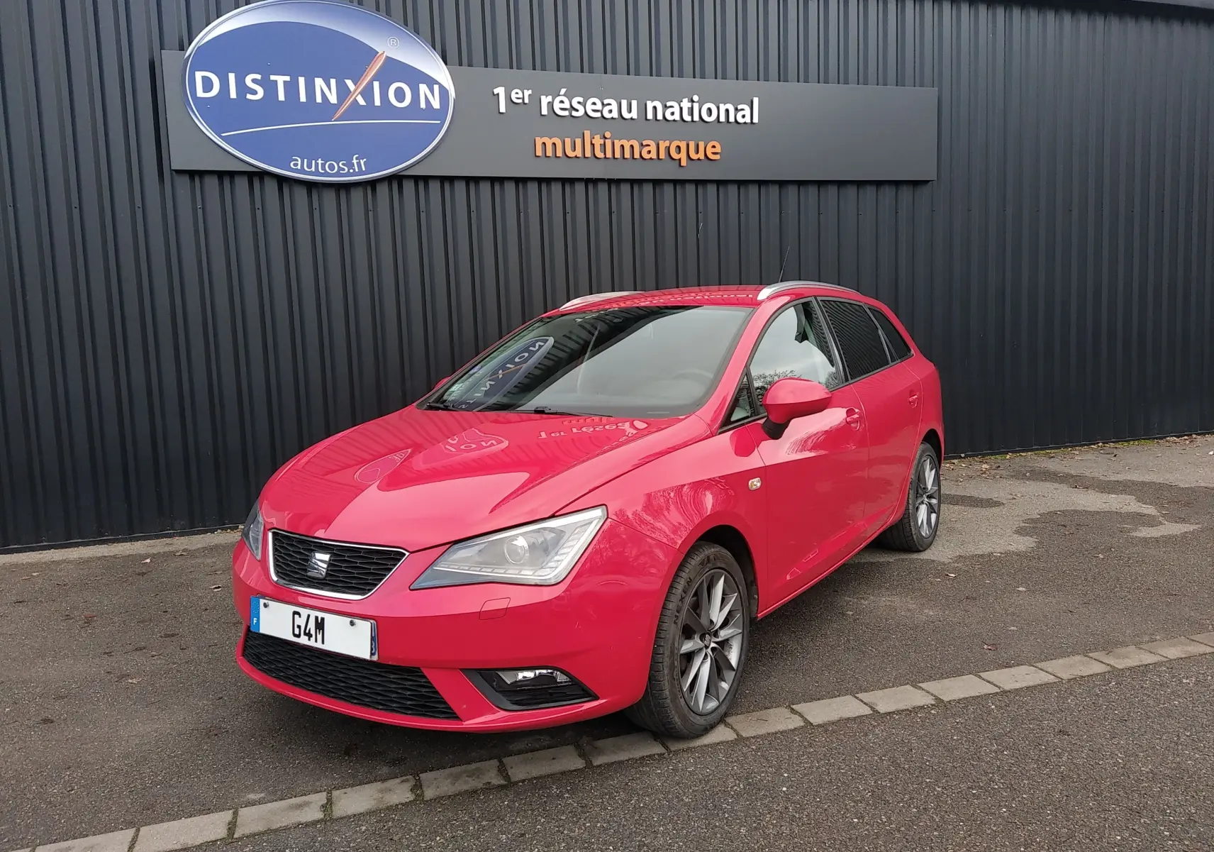 SEAT Ibiza ST rouge vue 3/4 avant droit, avec jantes alliage et phares Xenon, stationnée devant un mur noir.