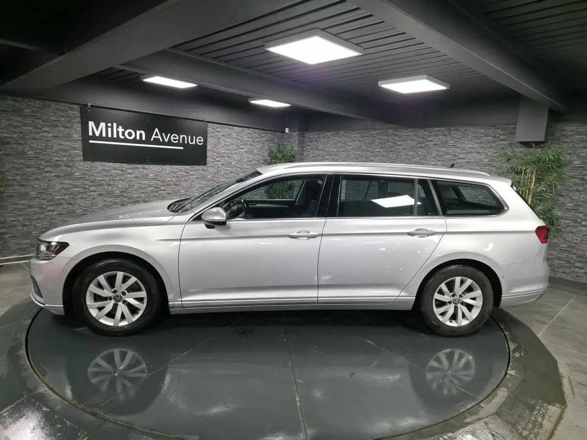 Volkswagen Passat SW gris métallisé vue de profil côté gauche dans un showroom avec mur en pierre grise.