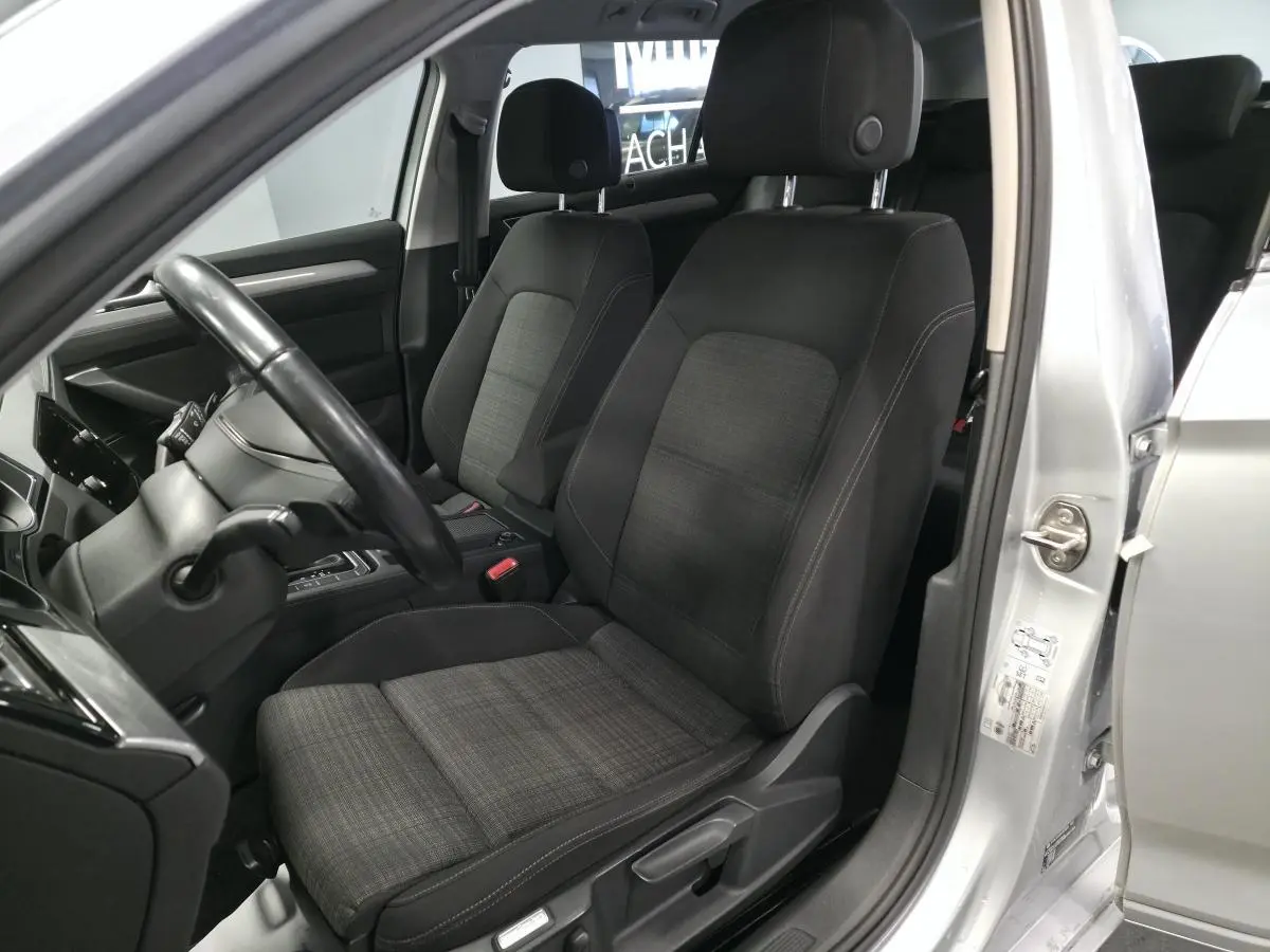 Vue intérieure côté conducteur d'une Volkswagen Passat SW 2021 gris, sièges tissu noir à motifs et volant cuir.