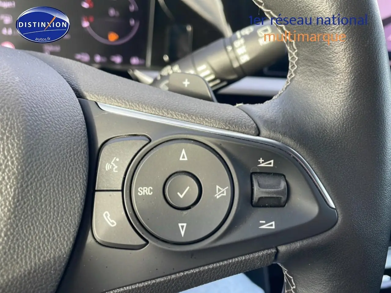 Gros plan sur les commandes audio et téléphone au volant cuir noir de l’Opel Grandland rouge hybride 2024.