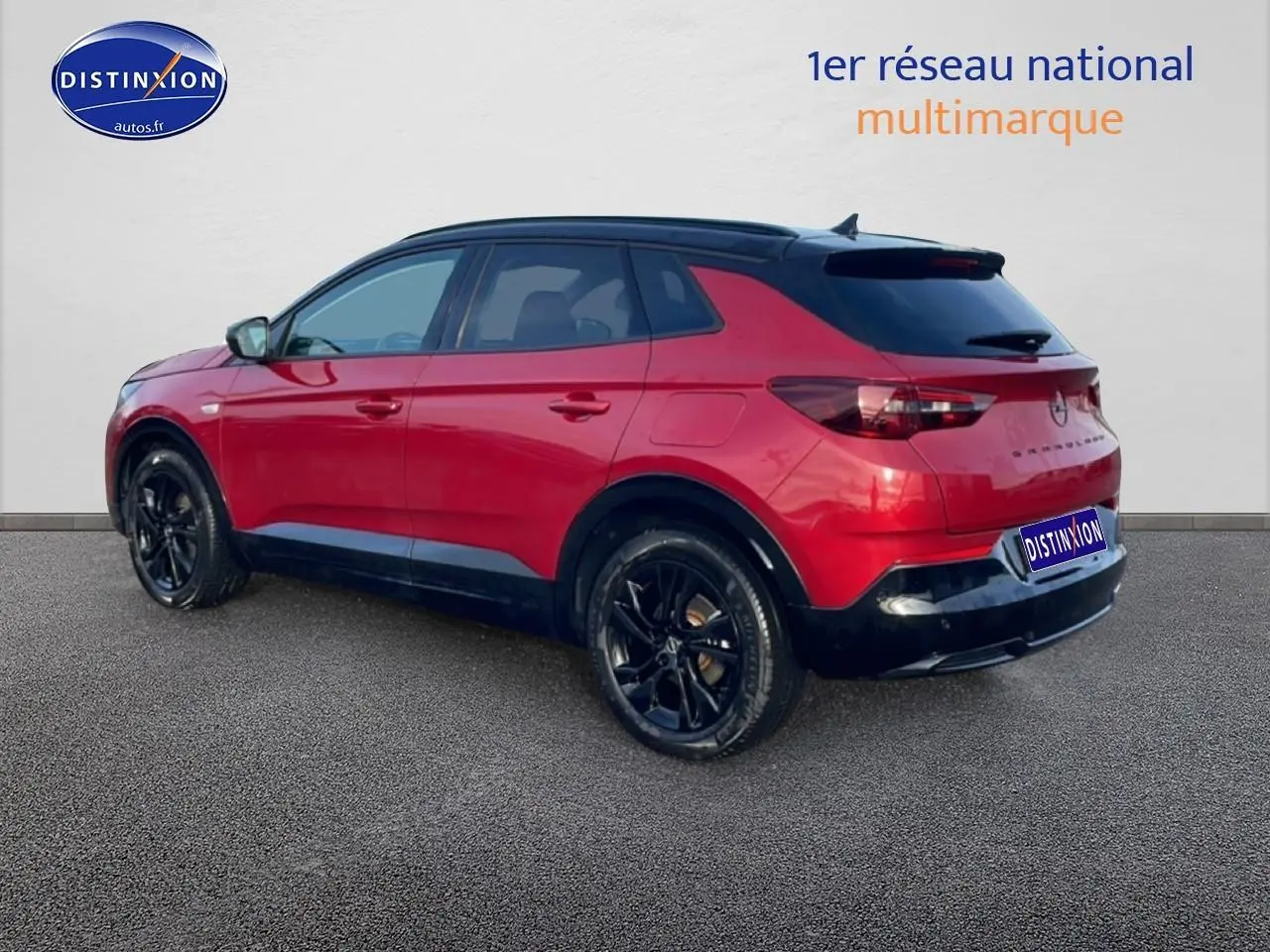 Vue 3/4 arrière droite d’un Opel Grandland rouge avec toit noir et jantes noires, sur fond neutre.