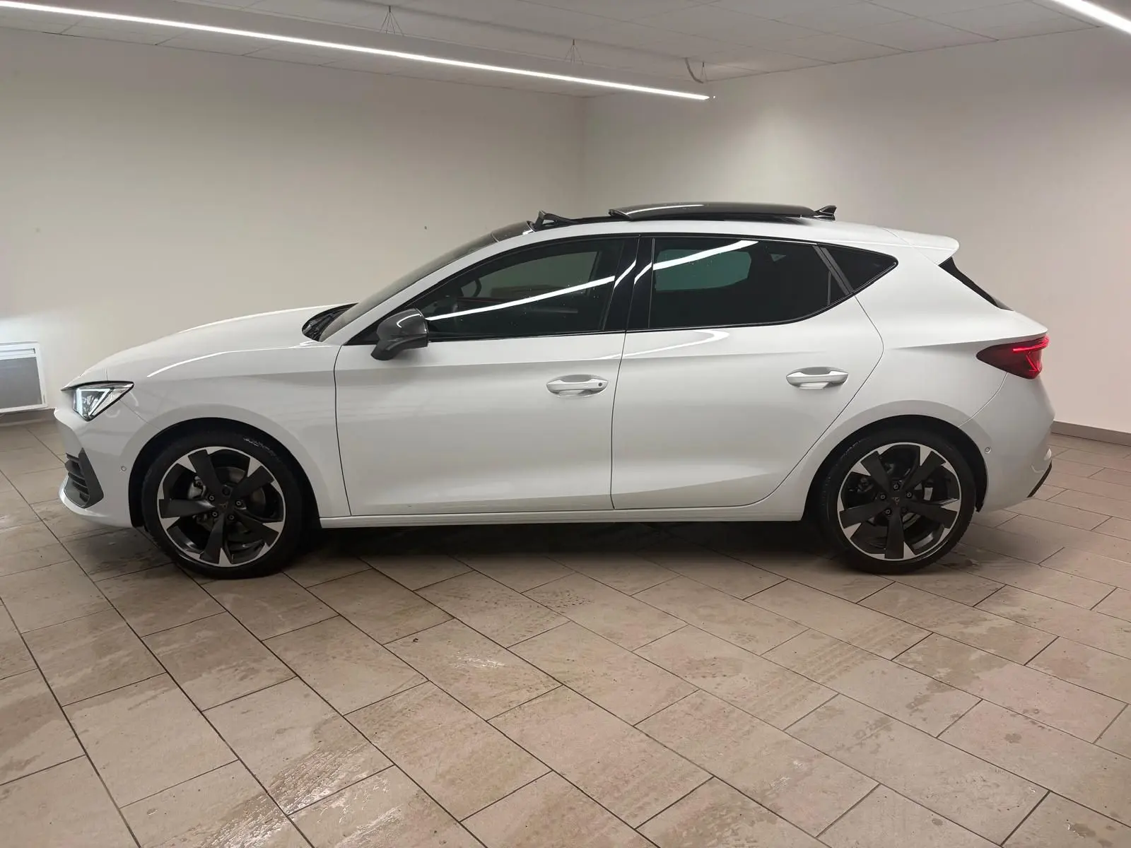 Vue de profil côté gauche d'une CUPRA Leon blanche Nevada avec toit ouvrant panoramique et jantes noires.