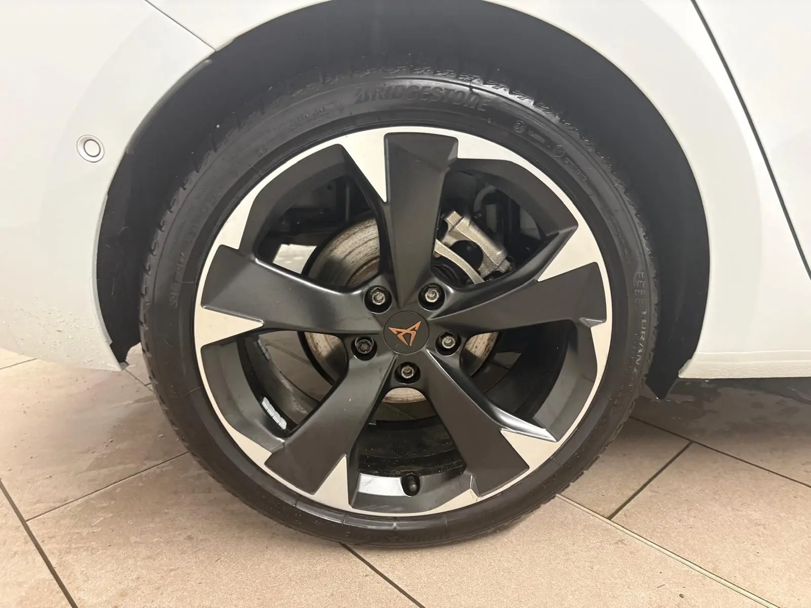 Gros plan sur la roue avant gauche de la CUPRA Leon blanche Nevada, avec jante noire et argent au design moderne.