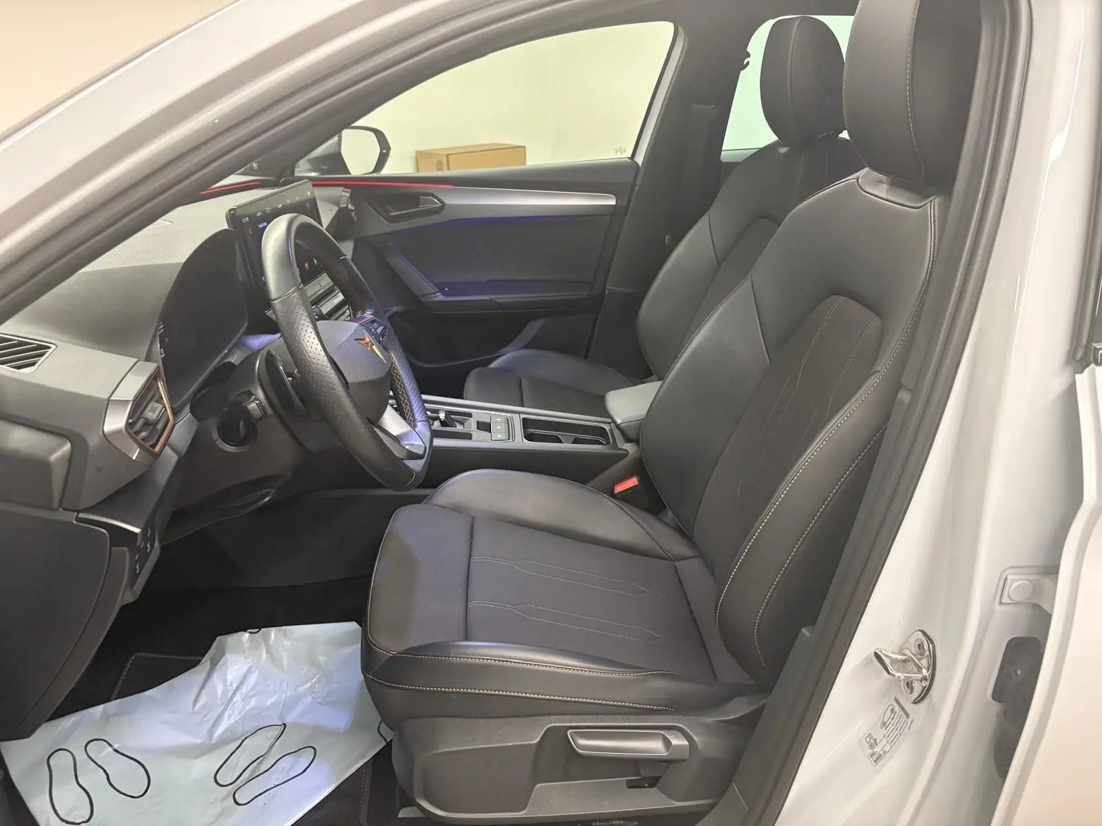 Intérieur avant droit de la CUPRA Leon blanc Nevada 2024, sièges noirs avec surpiqûres et volant multifonction.