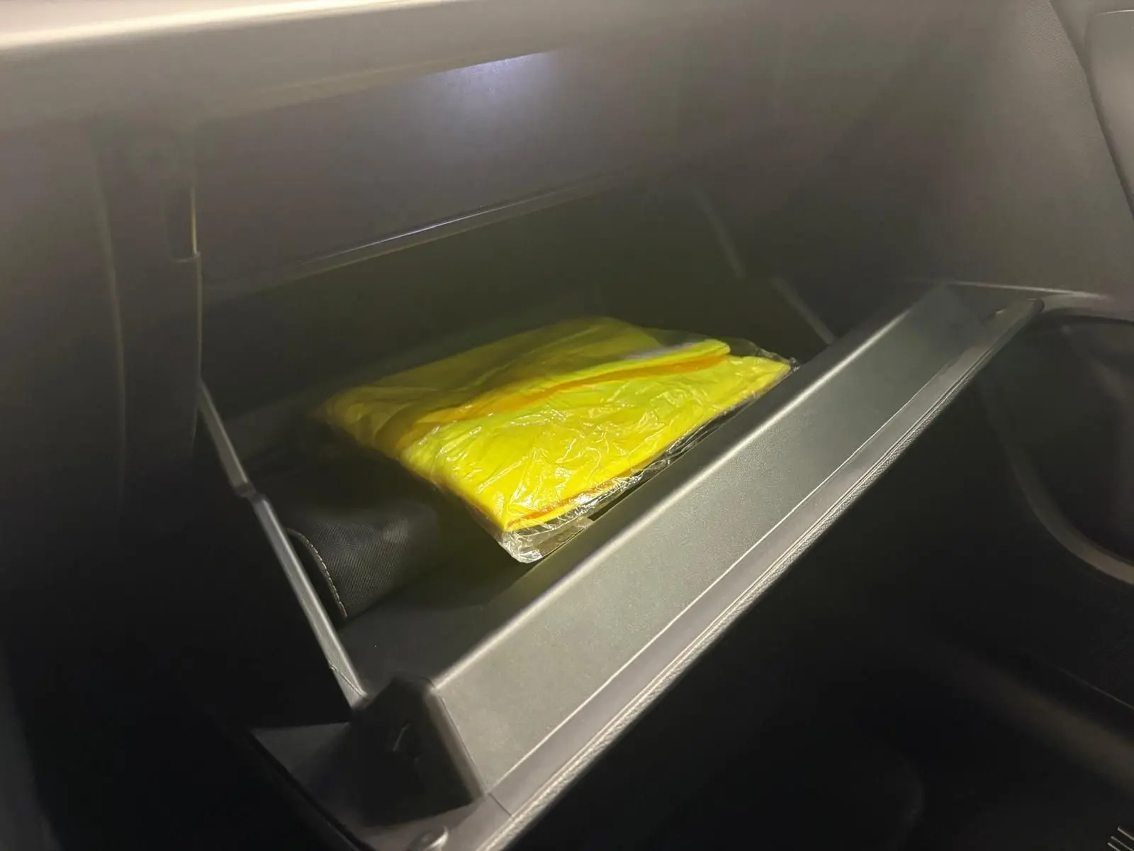 Gant de sécurité jaune dans la boîte à gants ouverte côté passager d'une CUPRA Leon 2024 blanc Nevada.