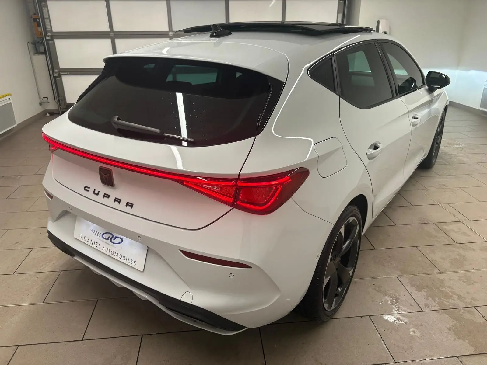 Vue 3/4 arrière droite d'une CUPRA Leon blanche Nevada avec toit ouvrant panoramique dans un garage.