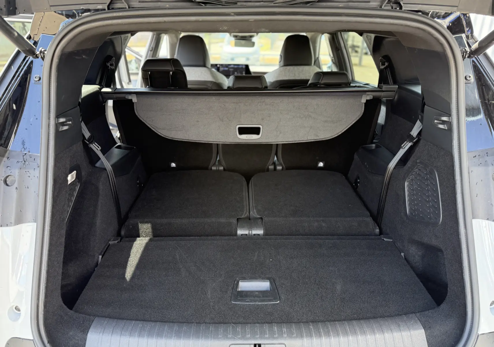 Coffre ouvert vu de l'arrière d'un Peugeot 5008 blanc Okenite avec banquette arrière rabattue et cache-bagages déployé.