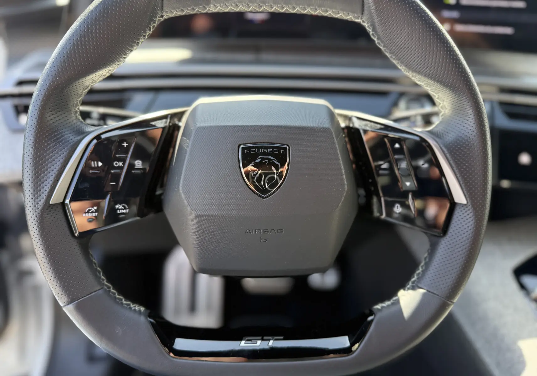 Vue rapprochée du volant cuir perforé du Peugeot 5008 Hybrid 145 GT, avec logo lion et commande multifonctions.