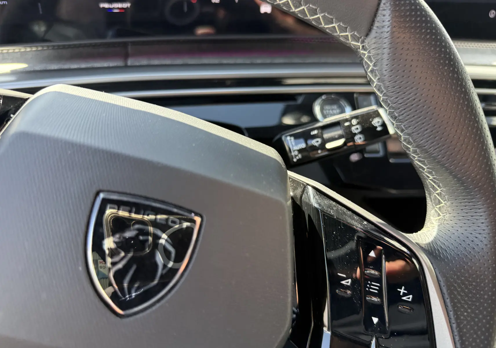 Gros plan sur le volant cuir perforé du Peugeot 5008 Hybrid 145 GT, avec commandes intégrées et logo lion central.