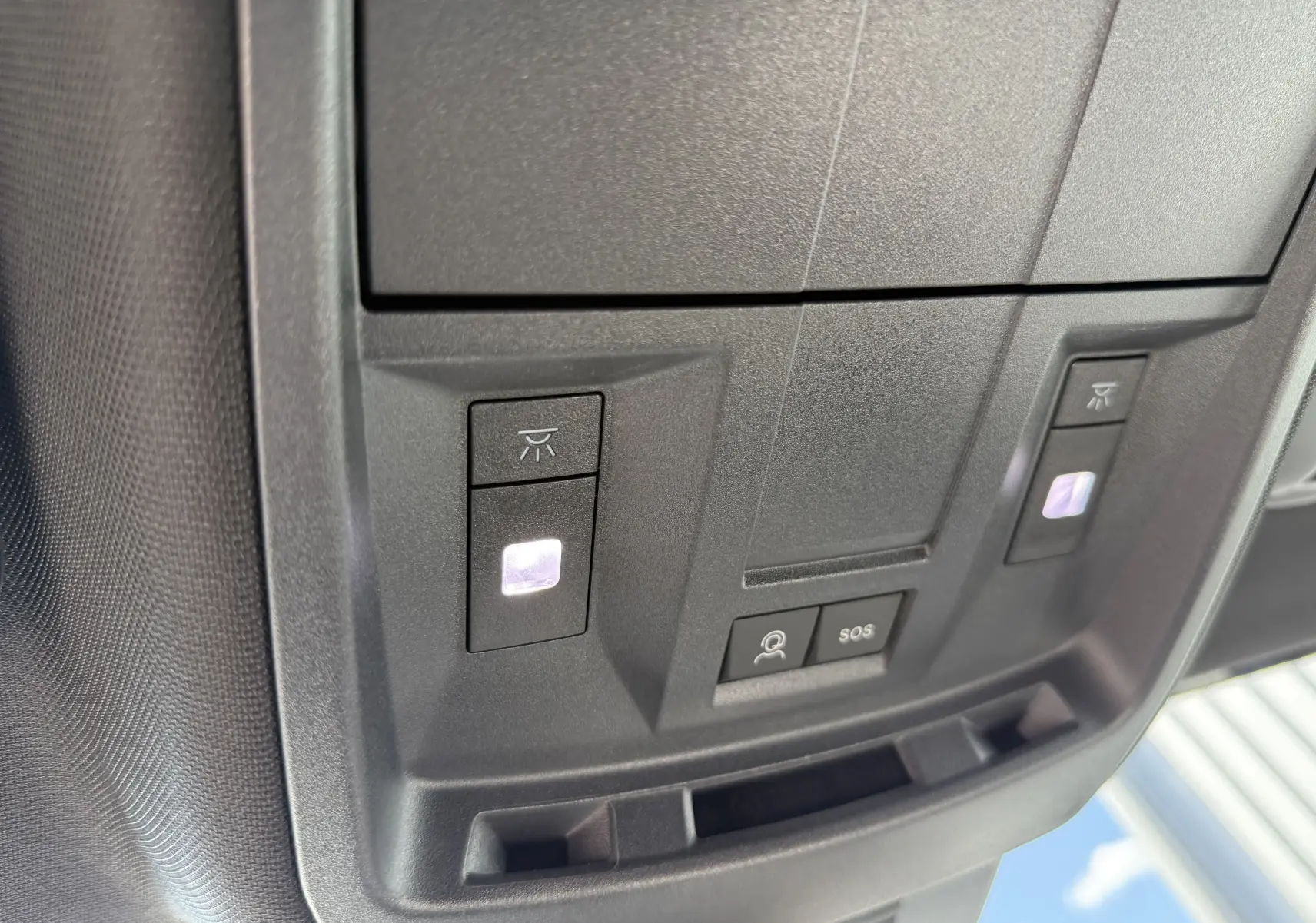 Gros plan sur la console de toit noire du Peugeot 5008 Hybrid 145 GT, avec boutons d’éclairage et SOS éclairés.