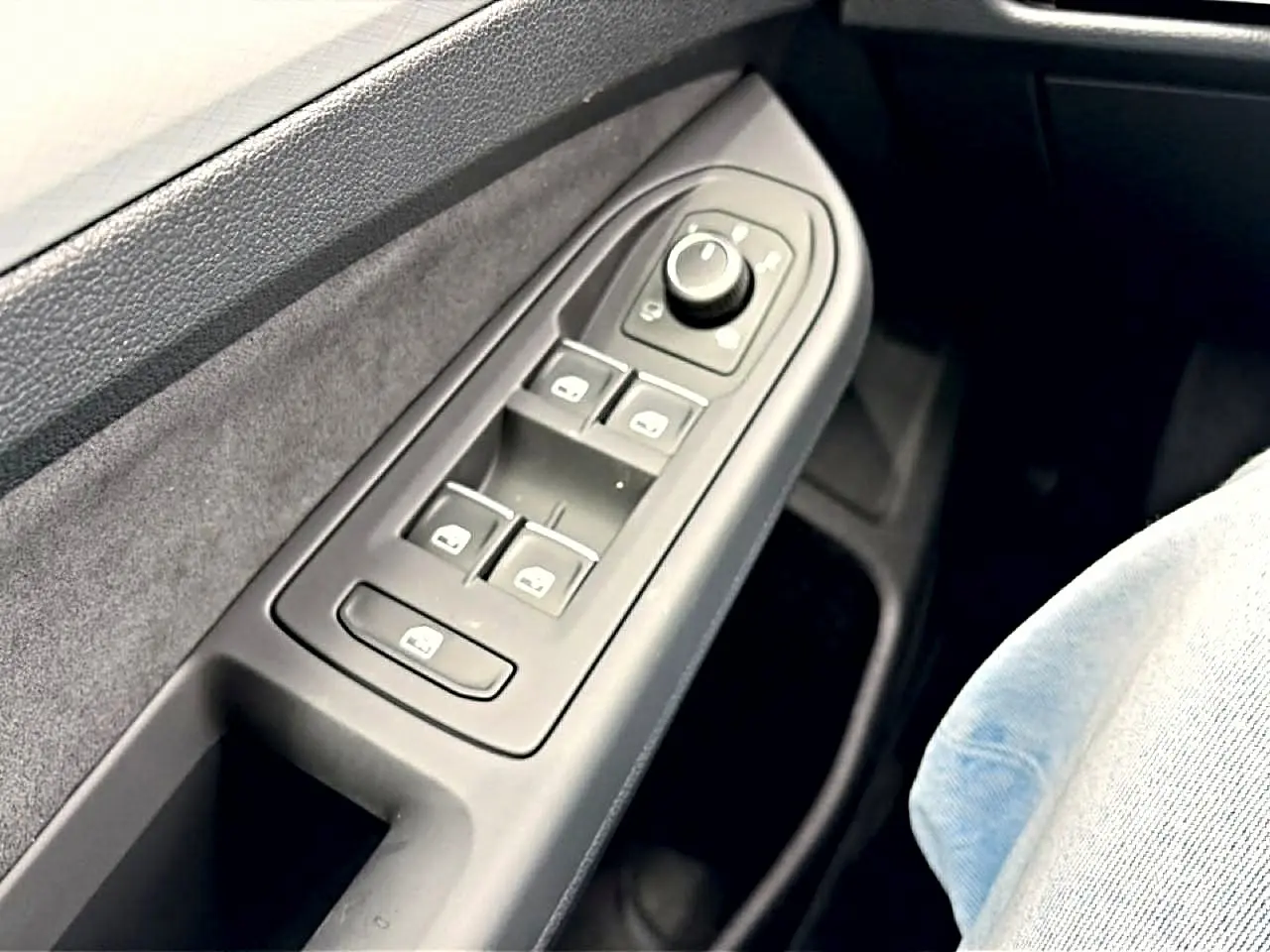 Gros plan sur la commande des vitres et rétroviseurs côté conducteur d’une Volkswagen Golf noire, intérieur gris.