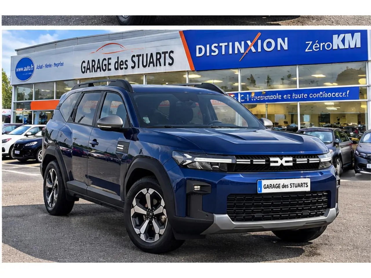 Dacia Bigster 2026 bleu indigo en 3/4 avant droit, avec jantes distinctives et toit noir, stationné devant un garage.