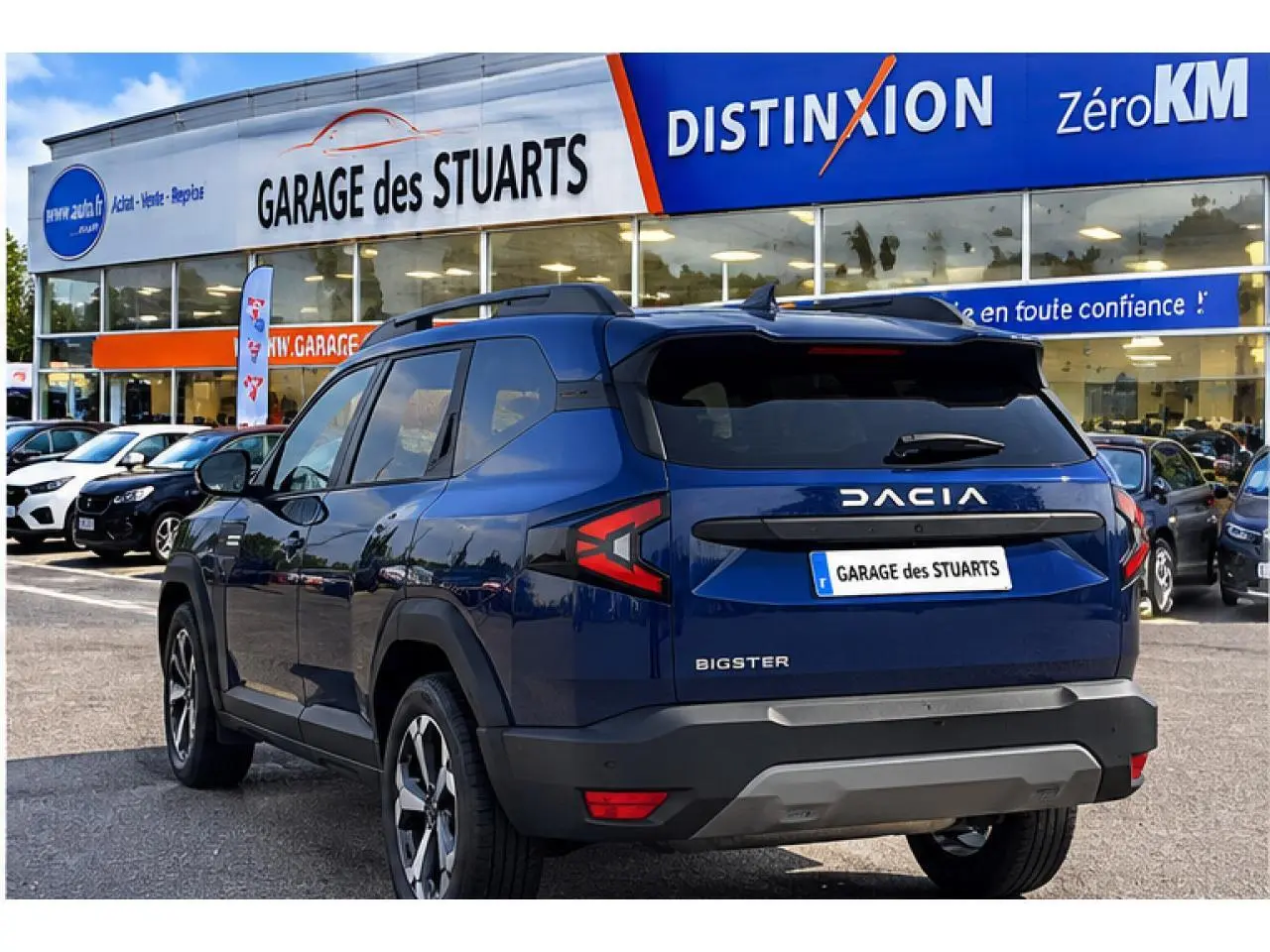 Vue 3/4 arrière droite du Dacia Bigster 2026 bleu indigo avec logo et plaque Garage des Stuarts visible.