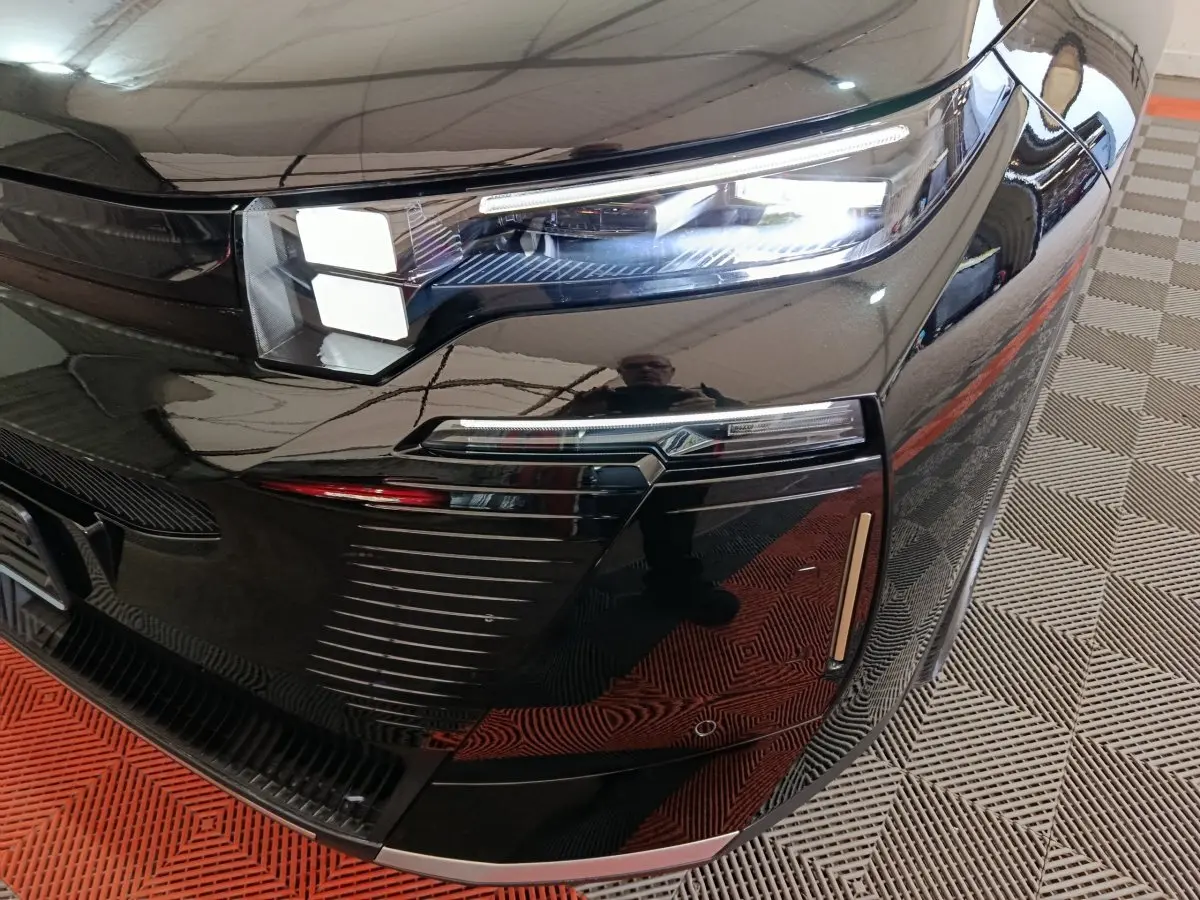 Gros plan sur le phare avant droit noir brillant du Citroën C5 Hybride 2026 avec éclairage LED et détails chromés.