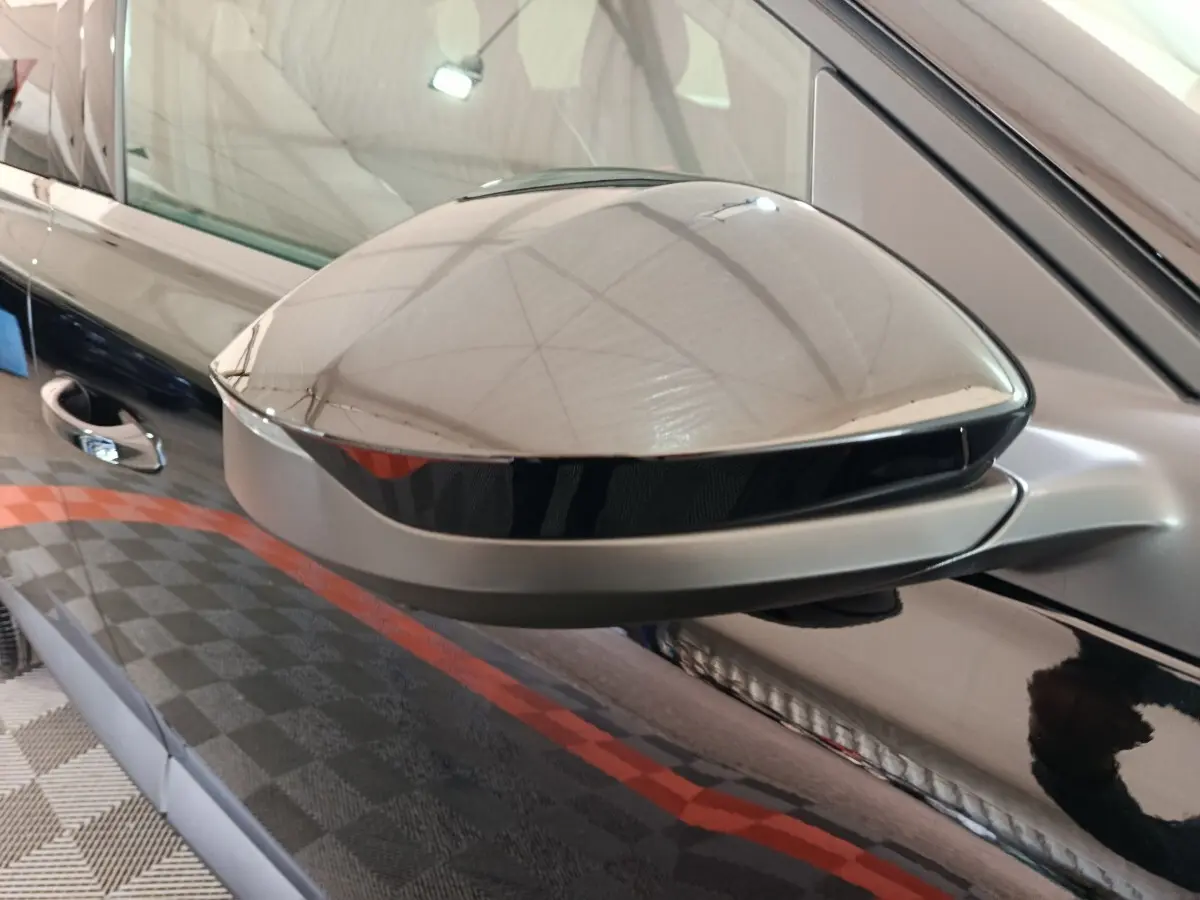 Gros plan sur le rétroviseur côté gauche noir brillant d'une Citroën C5 hybride 2026 avec portière noire en arrière-plan.