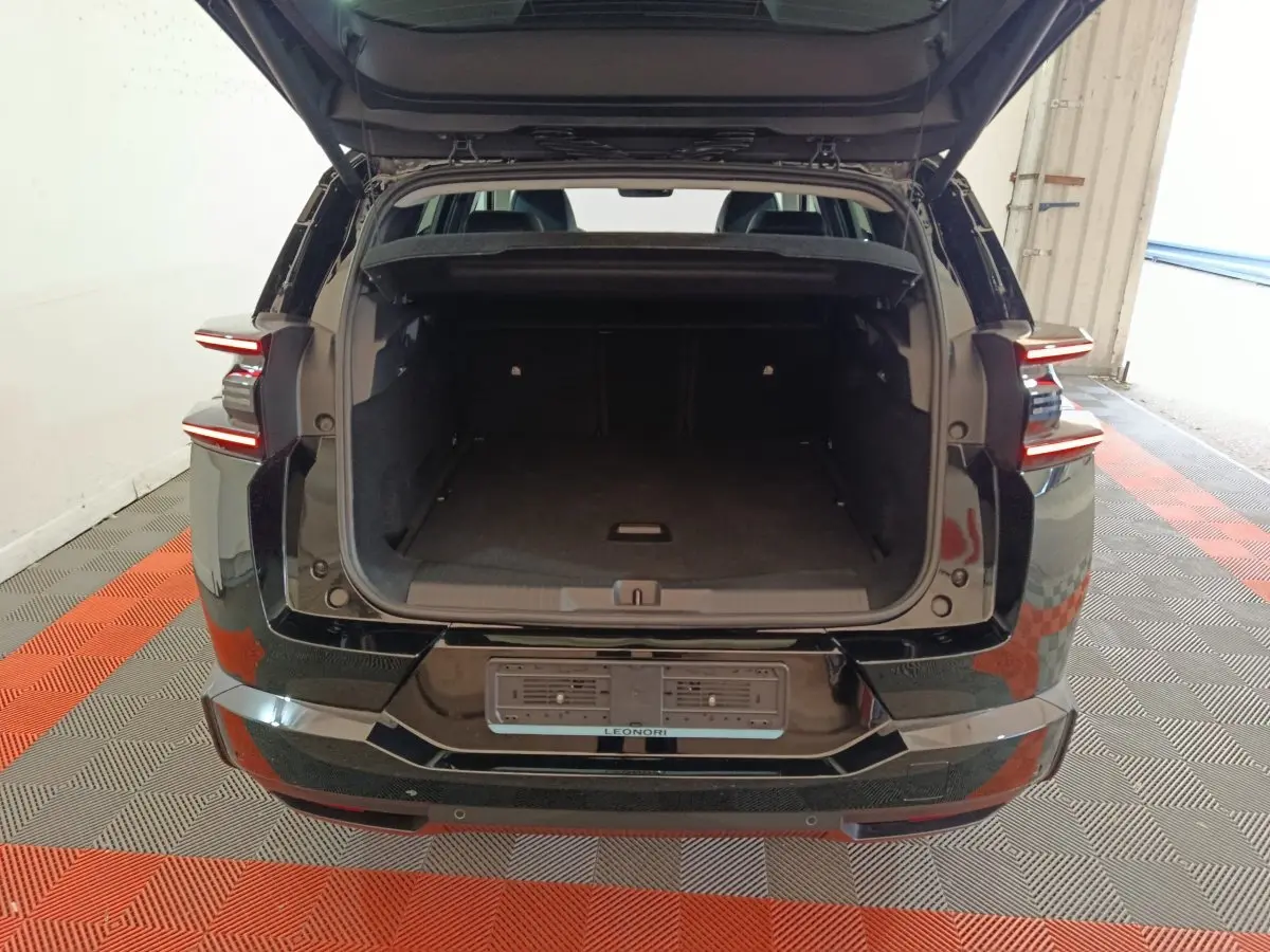 Vue arrière d'une Citroën C5 Hybride noire de 2026 avec coffre ouvert et feux arrière LED allumés.