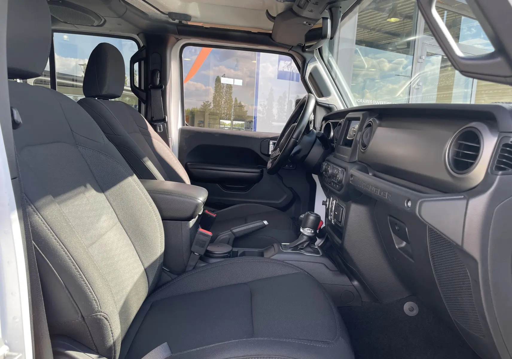 Intérieur avant droit du Jeep Wrangler blanc 2018, sièges tissu noir et tableau de bord avec volant multifonction.