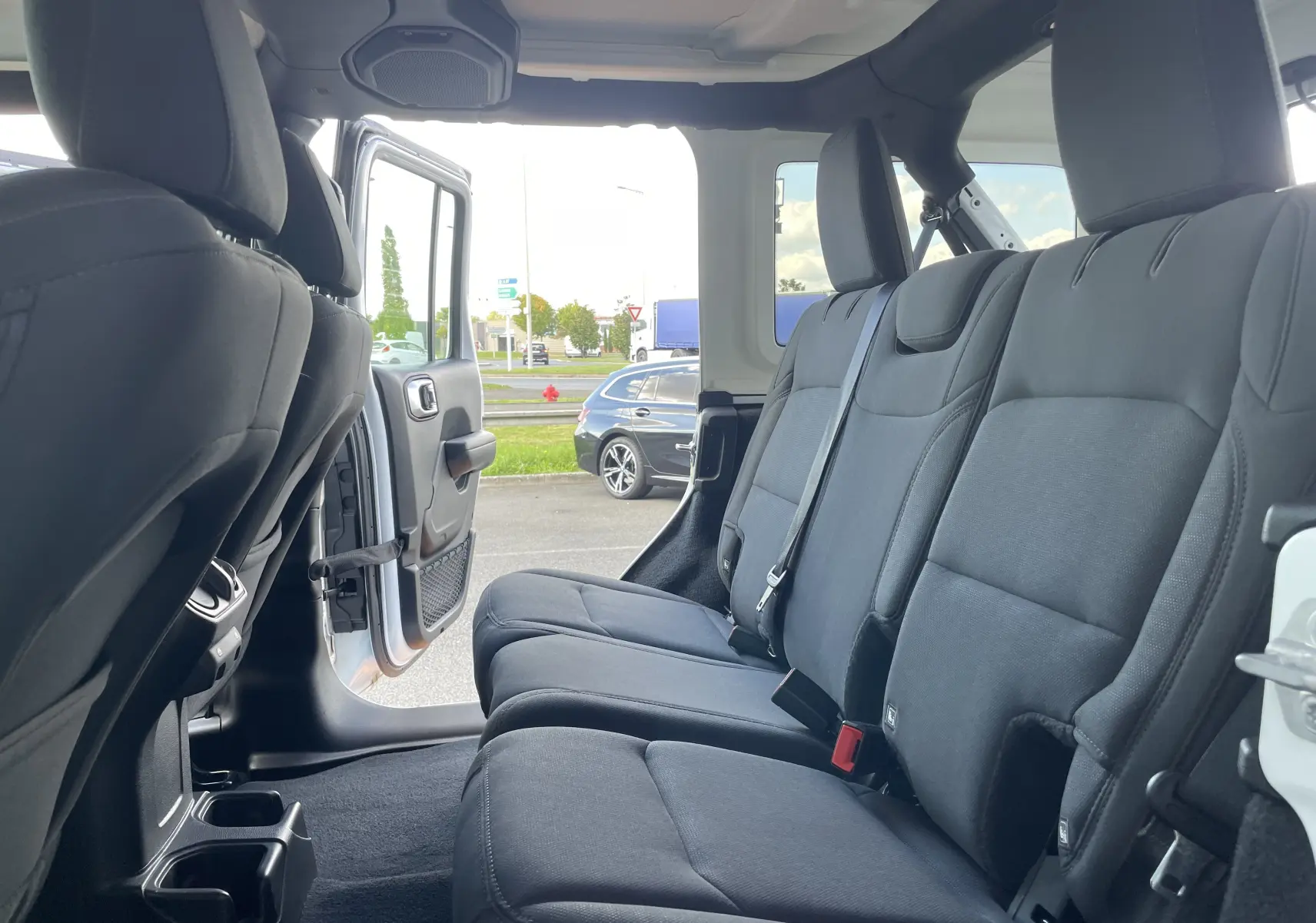 Vue intérieure côté droit sur les sièges arrière noirs en tissu d'un Jeep Wrangler blanc avec porte ouverte.
