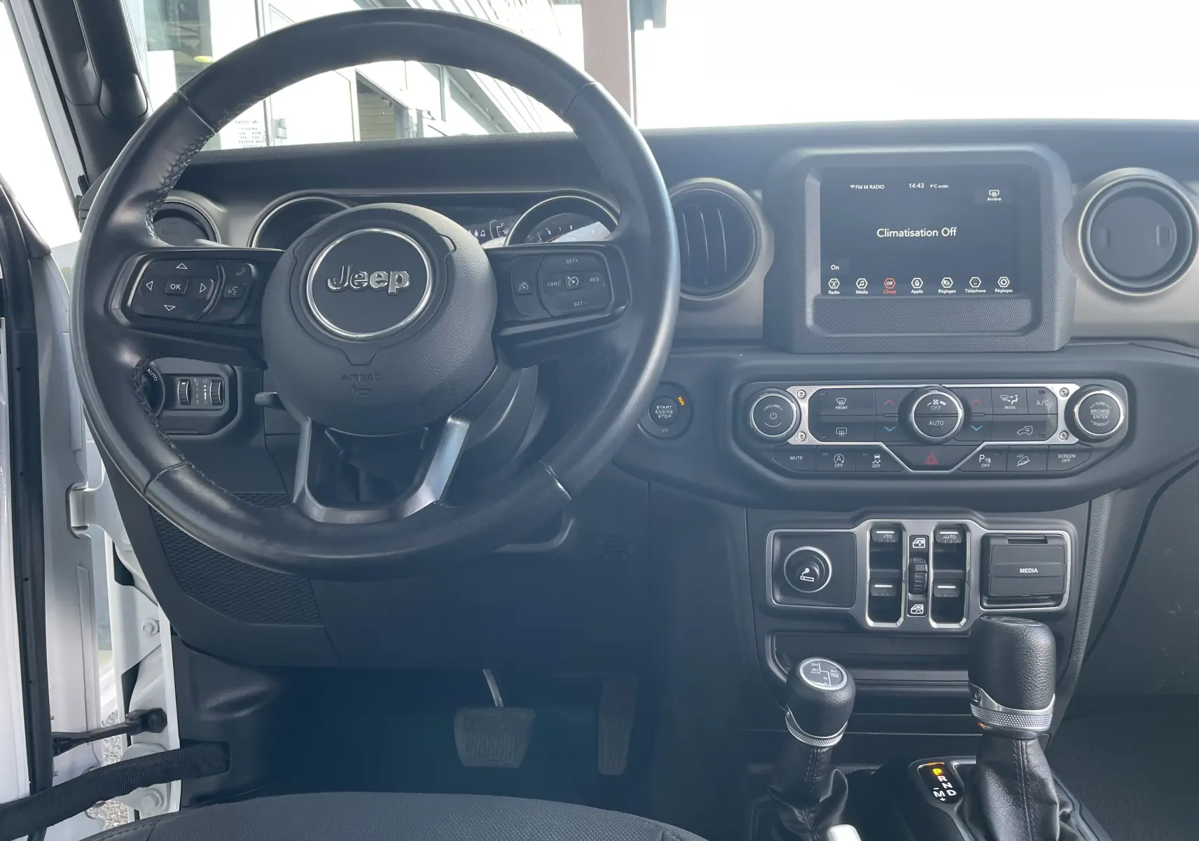 Vue intérieure centrée sur le volant Jeep noir et le tableau de bord avec écran tactile et commandes climatisation.