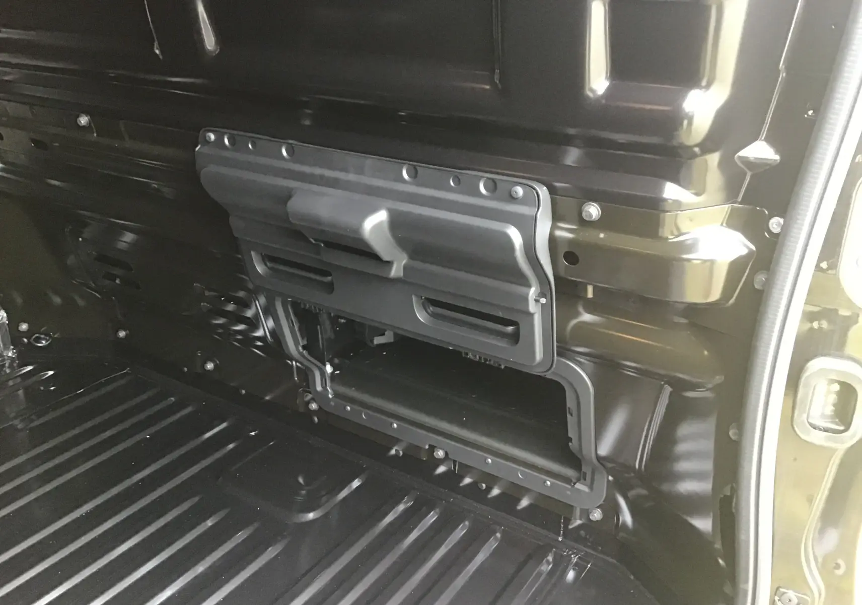 Vue intérieure du compartiment de chargement noir du Renault Trafic Fourgon L1H1, avec trappe de rangement ouverte sur la paroi latérale.