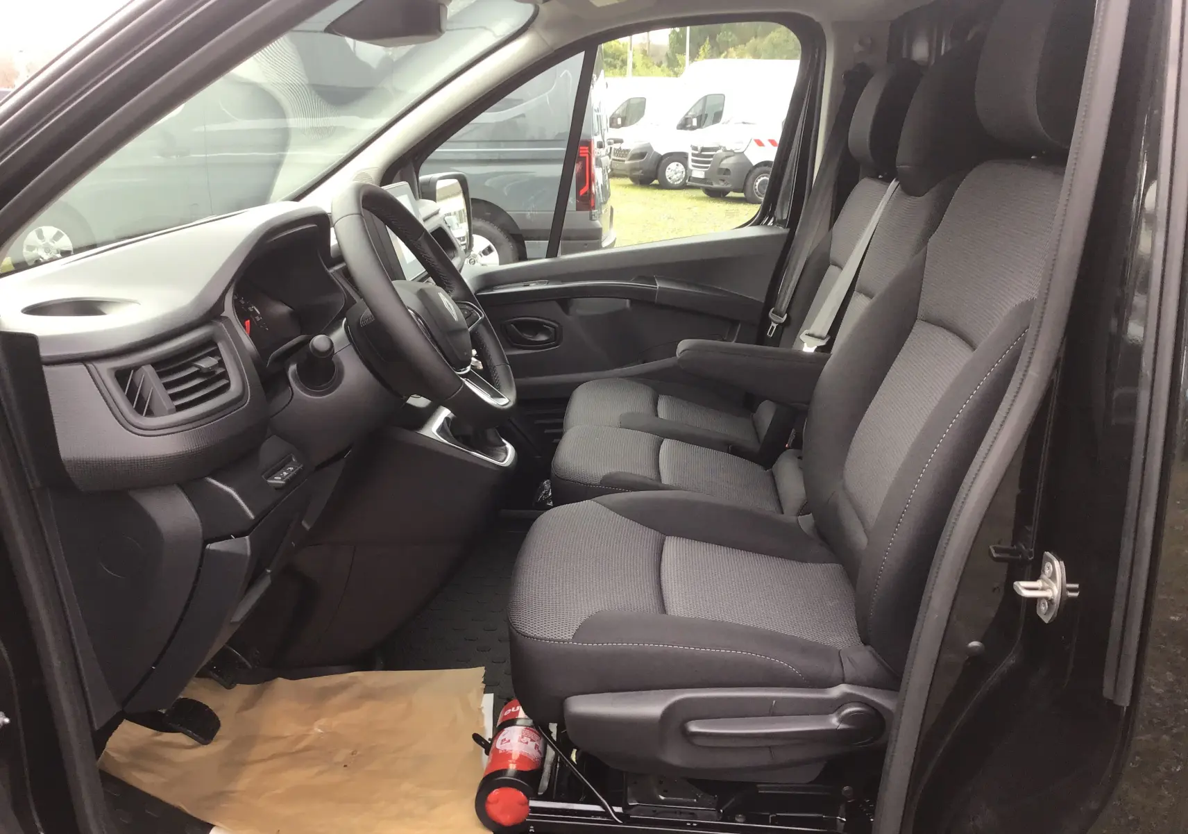 Vue intérieure côté conducteur du Renault Trafic Fourgon noir 2025, montrant les sièges avant et le tableau de bord.