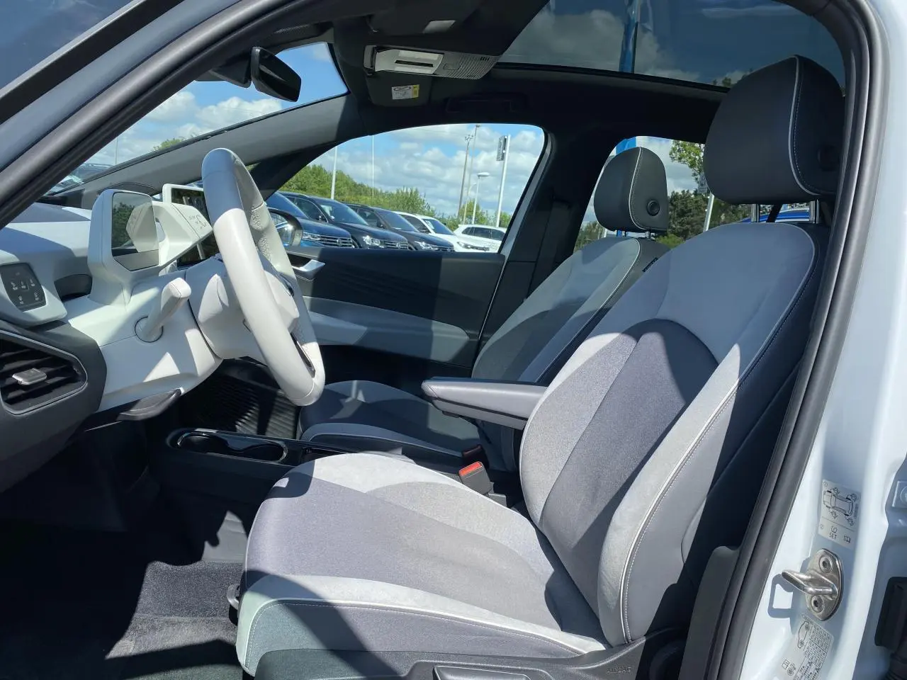 Intérieur avant droit d'une Volkswagen ID.3 blanc glacier, sièges tissu velours gris et toit vitré panoramique visible.