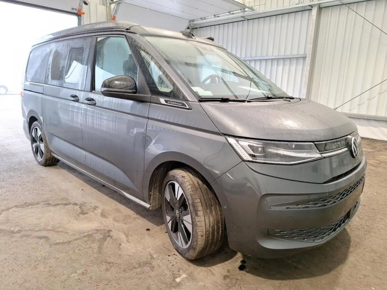 Vue 3/4 avant d’un Volkswagen California T7 gris Indium avec jantes alliage noir brillant et toit relevable fermé.