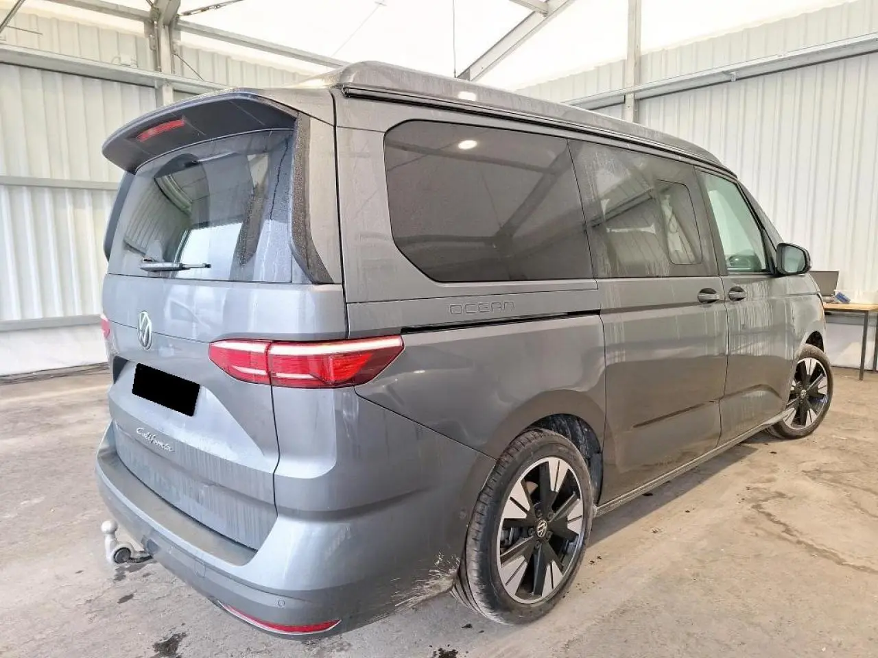 Vue 3/4 arrière droite du Volkswagen California T7 2.0 TDI gris Indium avec jantes alliage noir brillant et attelage rabattable.