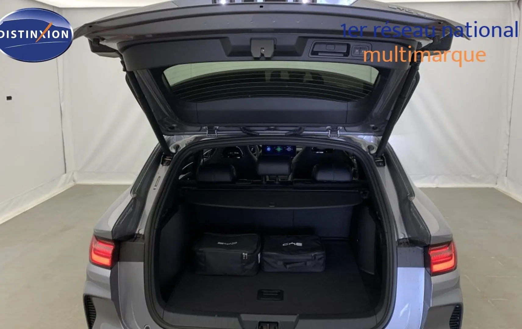 Vue arrière du coffre ouvert du BYD SEAL U Time Grey 2025 avec feux arrière LED allumés et deux sacs de rangement à l’intérieur.