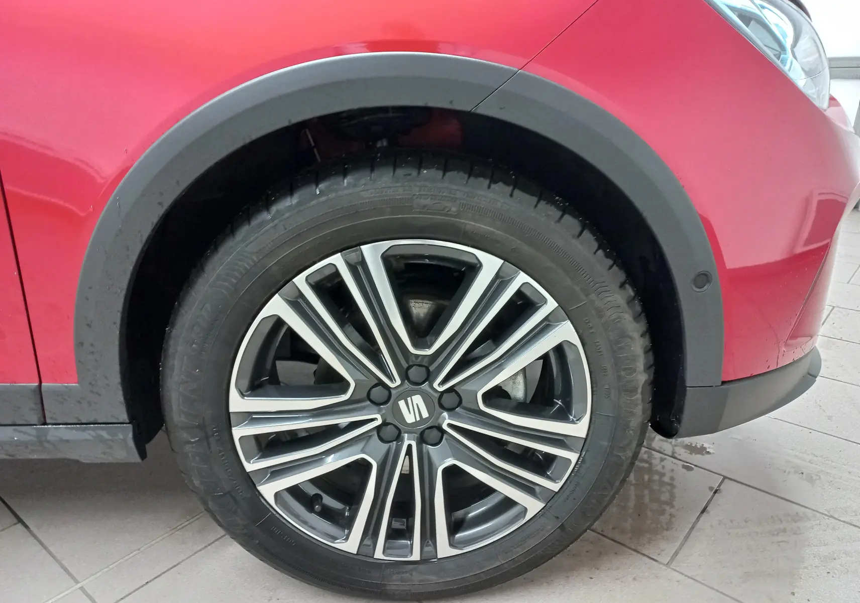 Gros plan sur la roue avant droite d’un SEAT Arona rouge Désir avec jante alliage bicolore et entourage noir.